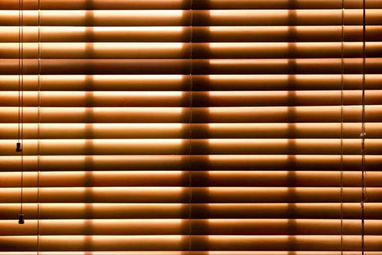 A view of closed brown mini blinds with the sun coming through.