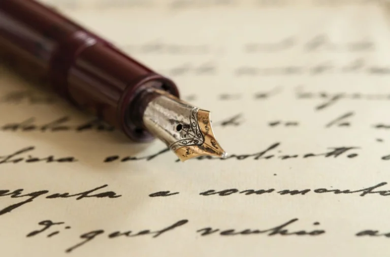 A close-up of a retro-style fountain pen lying on a piece of textured paper with calligraphy writing on it.