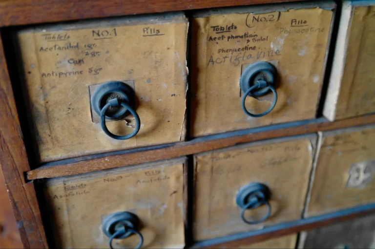 A close-up view of vintage pharmaceutical prescription filing cabinet drawers with writing on them.