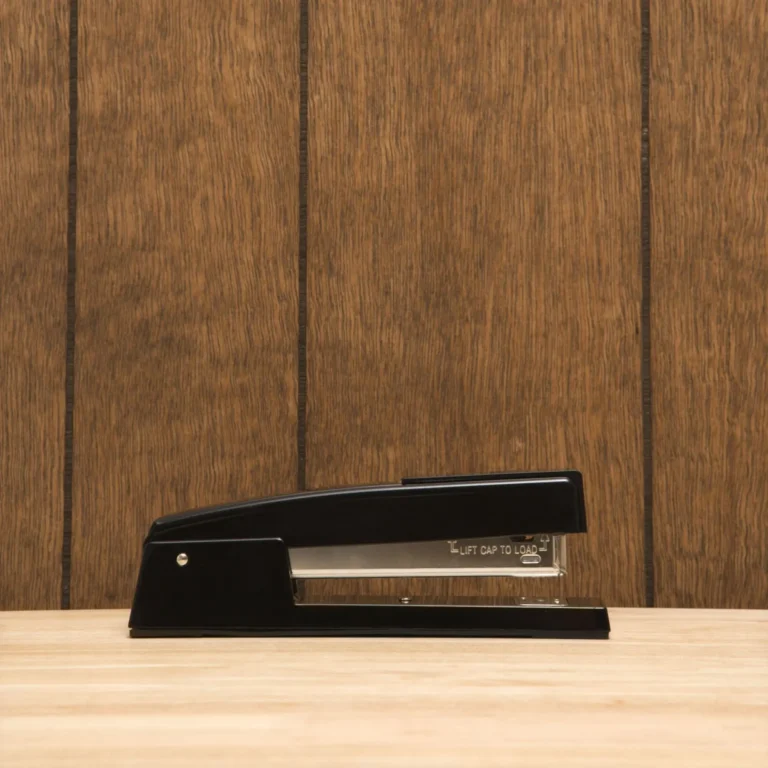 A black vintage stapler with vintage wooden panels in the background.