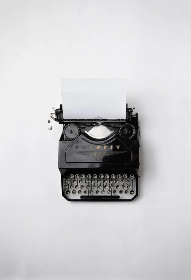 A top-view of a black, old-fashioned typewriter set against a white surface.