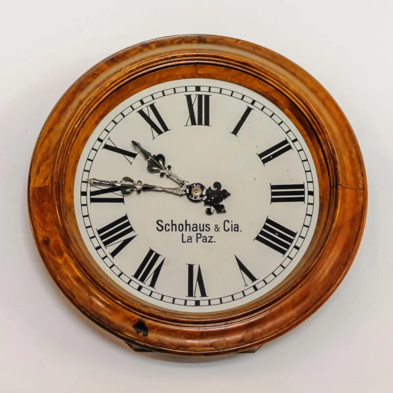 A frontal view of a round antique clock in a wooden frame, with Roman numerals.