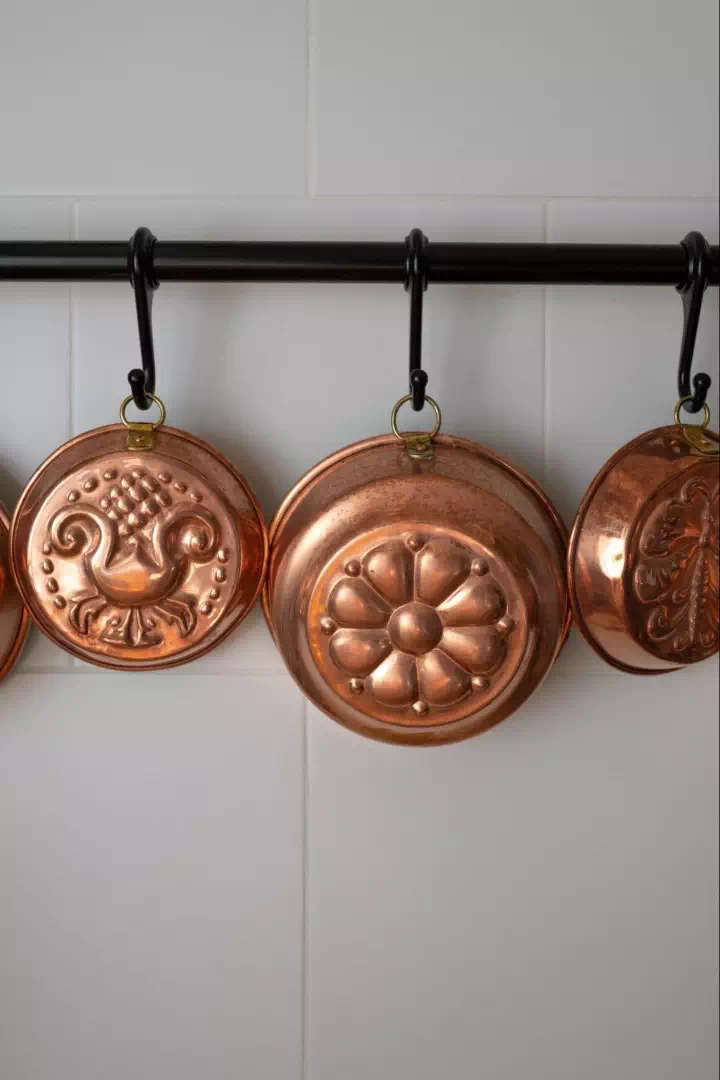 Three decorative copper pans hanging against a white-tiled wall.