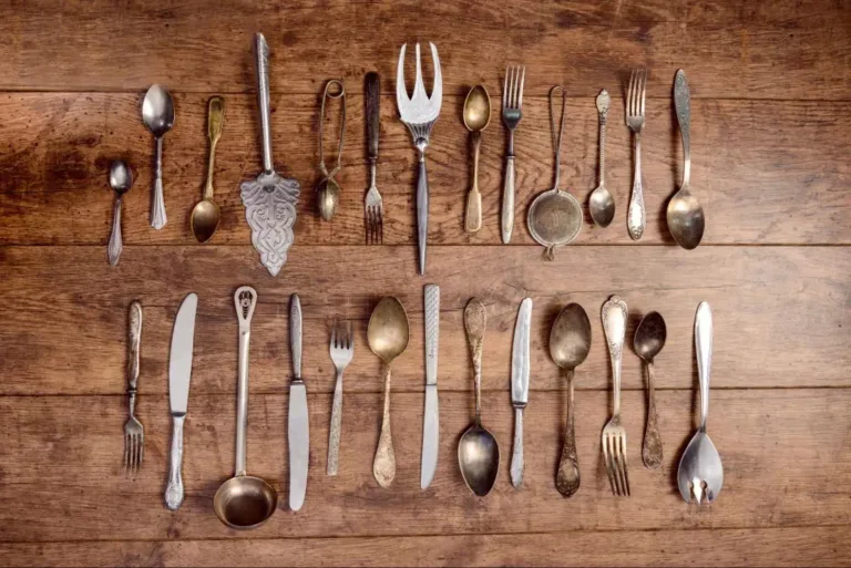 A collection of Victorian silverware including forks, knives, spoons, and a cake and pie server, laid out on a wooden surface.