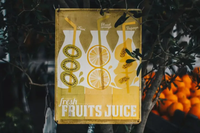 A rectangular, green and yellow vintage sign reading “Fresh Fruits Juice” featuring illustrations of kiwis, oranges, and papayas.