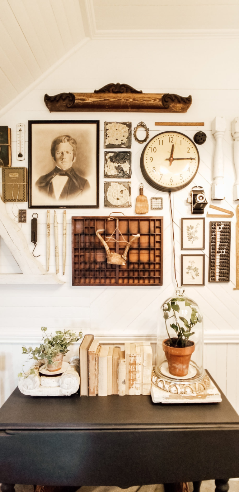 A vintage farmhouse gallery wall featuring old farm implements, a black and white photograph, a vintage clock, vintage books, and a plant in a glass cloche.