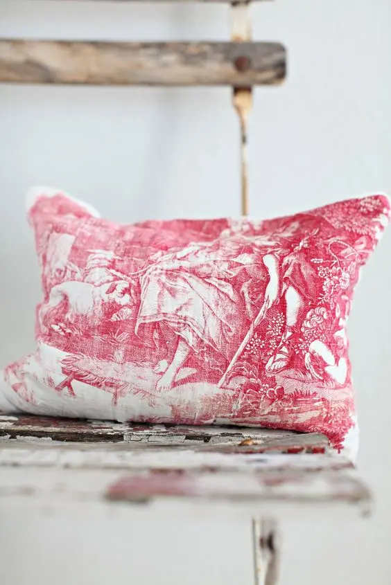 A red and white vintage French toile pillow placed on a distressed shabby rustic surface.