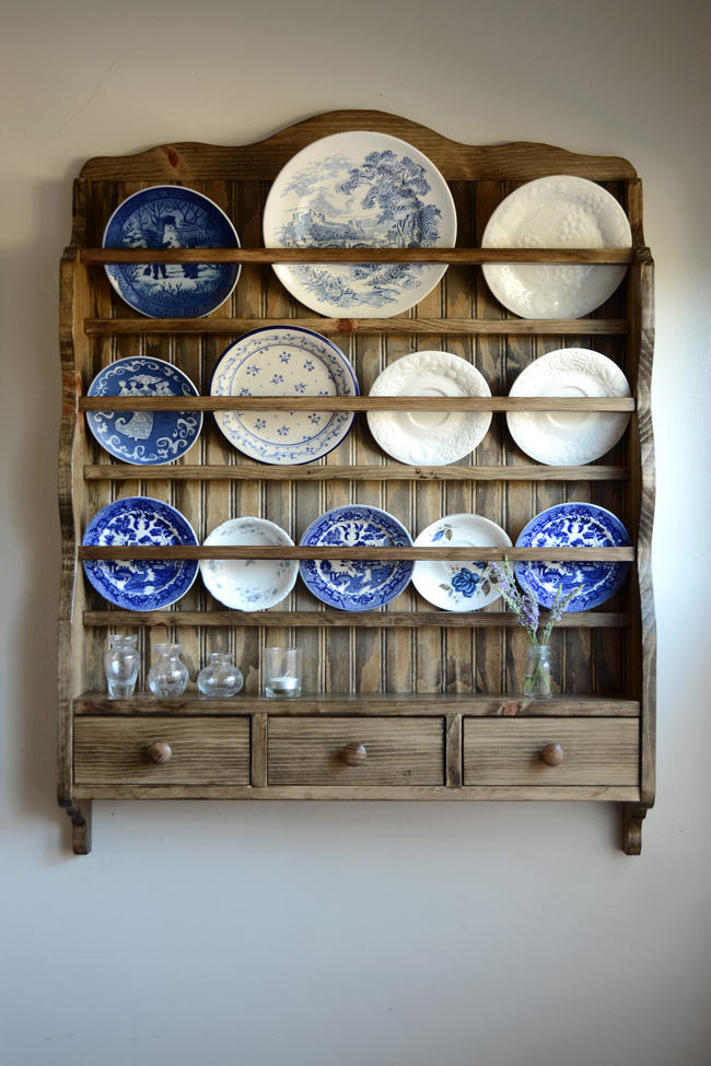 A dark wood vintage plate rack with three drawers, displaying various round blue and white blue willow plates.