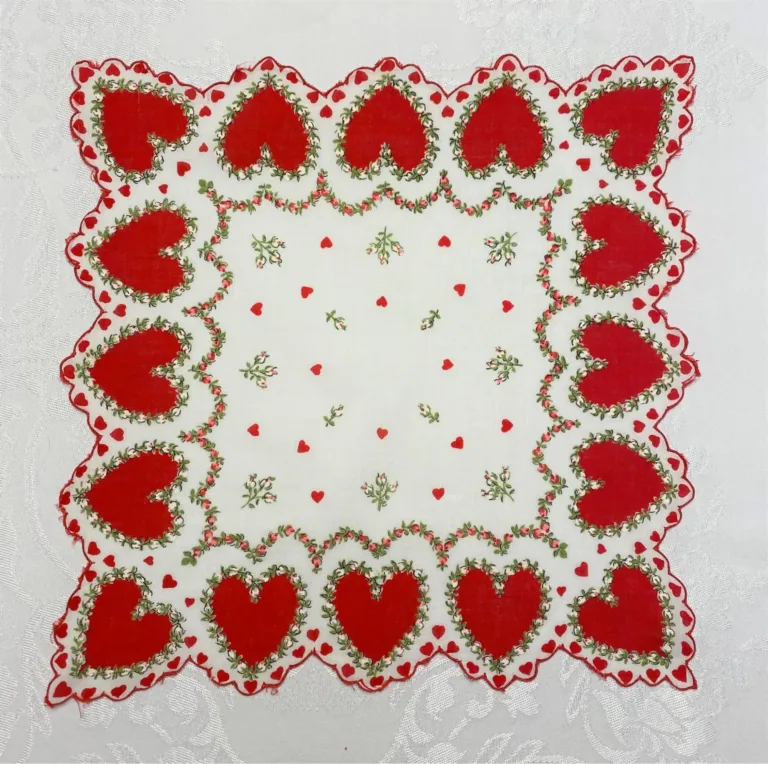 An embroidered vintage Valentine linen framed with hearts and floral motifs, spread out on a vintage white tablecloth.