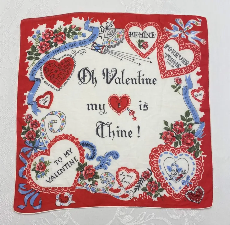 A vintage Valentine handkerchief decorated with ornamental hearts with messages reading ‘To my Valentine’, ‘I love you’, ‘Be Mine’, and more decorative elements such as cupids, doves, and blue bows.