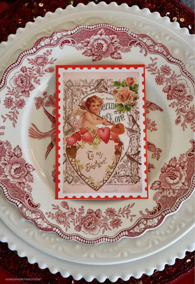 A vintage Valentine’s Day card with a cupid, a heart, and roses sitting on top of a vintage red and white plate.