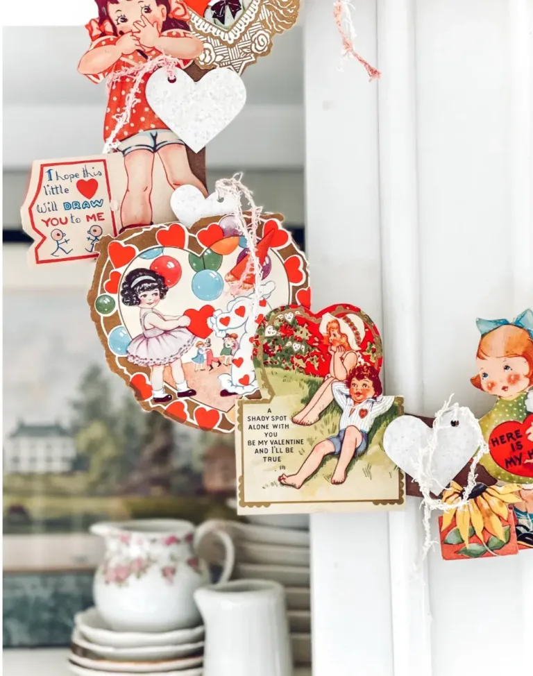 A closeup of a vintage Valentine wreath made up of vintage Valentine cards, hanging on a vintage kitchen cabinet.