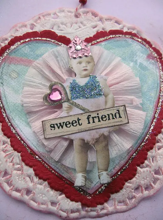 A vintage Valentine heart-shaped decoration made up of a vintage photo of a baby with a sparkly crown and glitter.