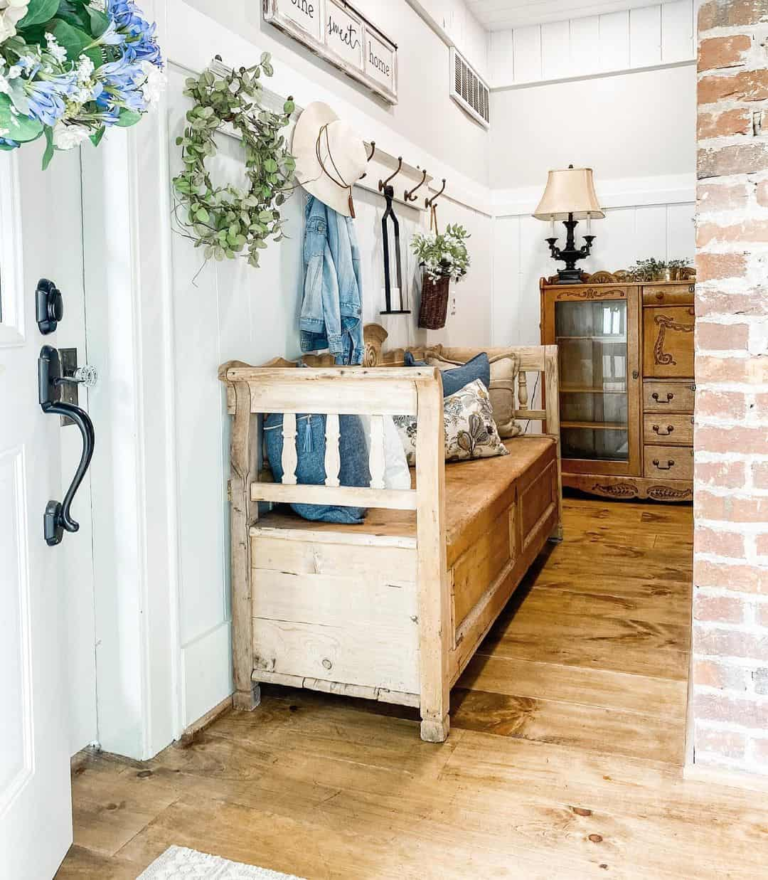 A vintage farmhouse kitchen with a rustic white table, cabinet with white plates, wicker containers and a vintage farmhouse sign reading Antiques.