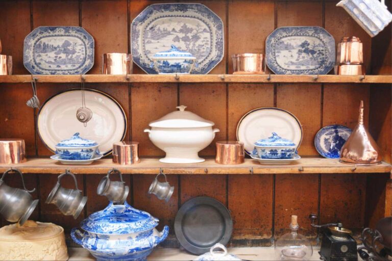 A display of blue and white china, and porcelain and pewter dishes in a vintage farmhouse open-shelved cabinet.