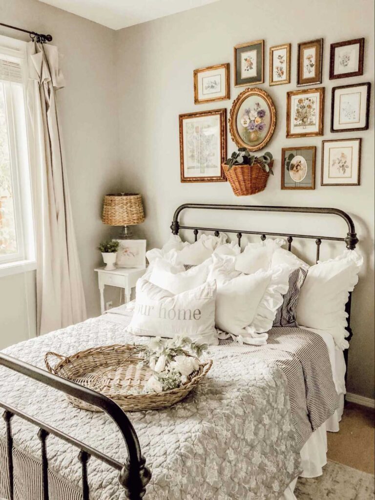 A gallery wall made up of old flower illustrations in antique square, rectangular, and oval frames hangs above an iron-frame bed with white pillows and a vintage sage green quilt.