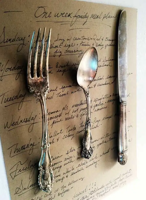 An antique fork, teaspoon, and dinner knife are mounted onto a brown-colored page with black calligraphy notes on it.