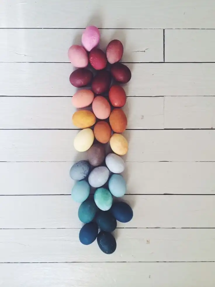 Colorful dyed Easter eggs arranged vertically according to color from light pink at the top to dark blue at the bottom, laid on a white wooden surface.