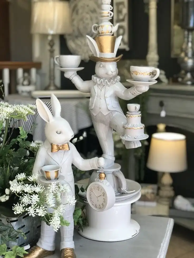 Two vintage white and gilded bunny figurines – one holding a clock and a teacup and the other holding teacups and a tray of cakes.