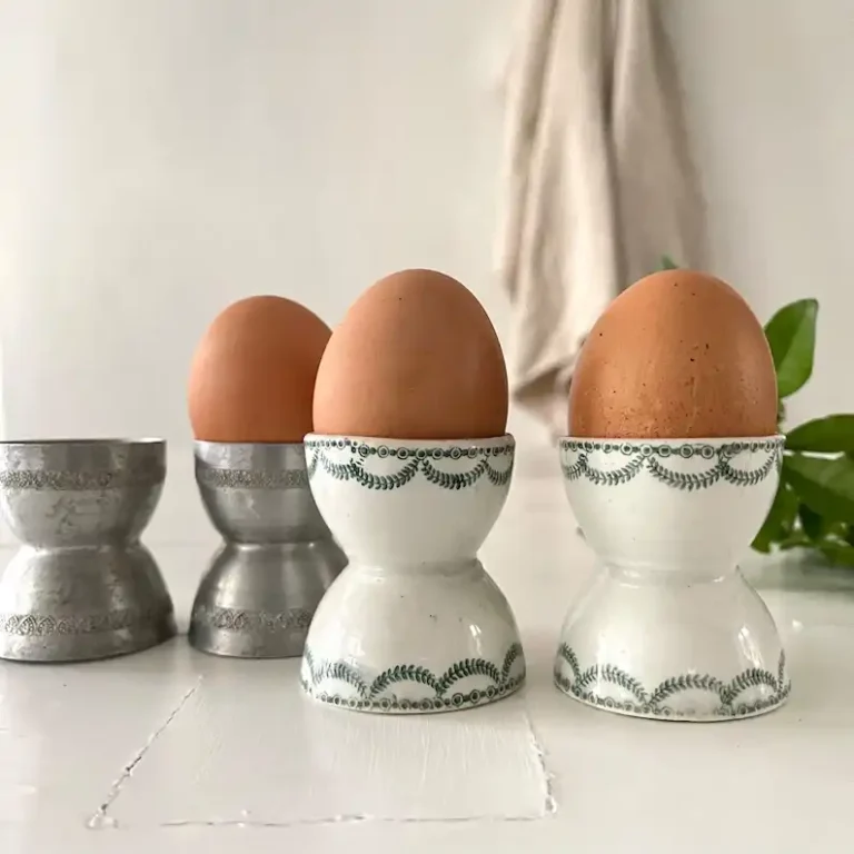 Four vintage Easter egg cups with an egg in three cups and one empty cup.