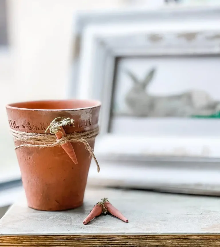 A rustic clay rust-colored flower pot with twine and a clay carrot decoration tied around it.