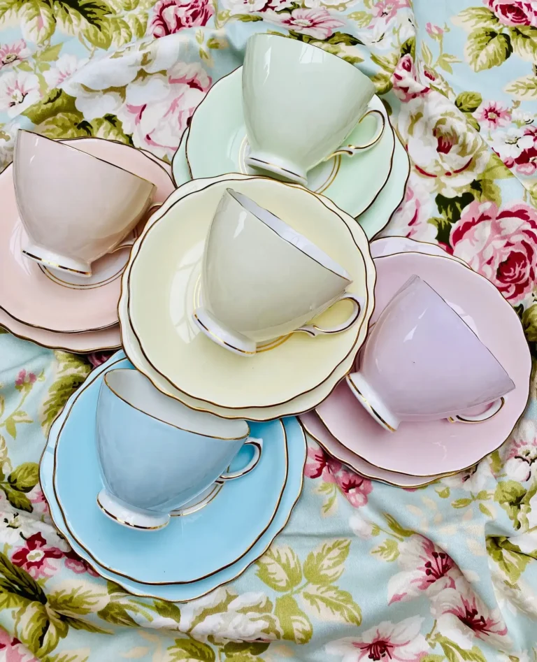 Five different-colored vintage pastel teacups each sitting on two round matching plates.