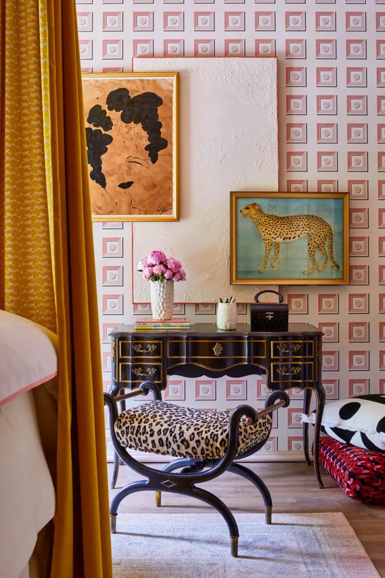 A leopard print-upholstered stool on rounded dark wood legs stands in front of a black and gold Louis IV dresser and a leopard painting hangs on a wall in the background.