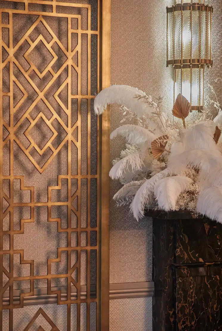 A partially visible gilded Art Deco room divider next to a white ostrich feather centerpiece placed on a black and gold countertop.