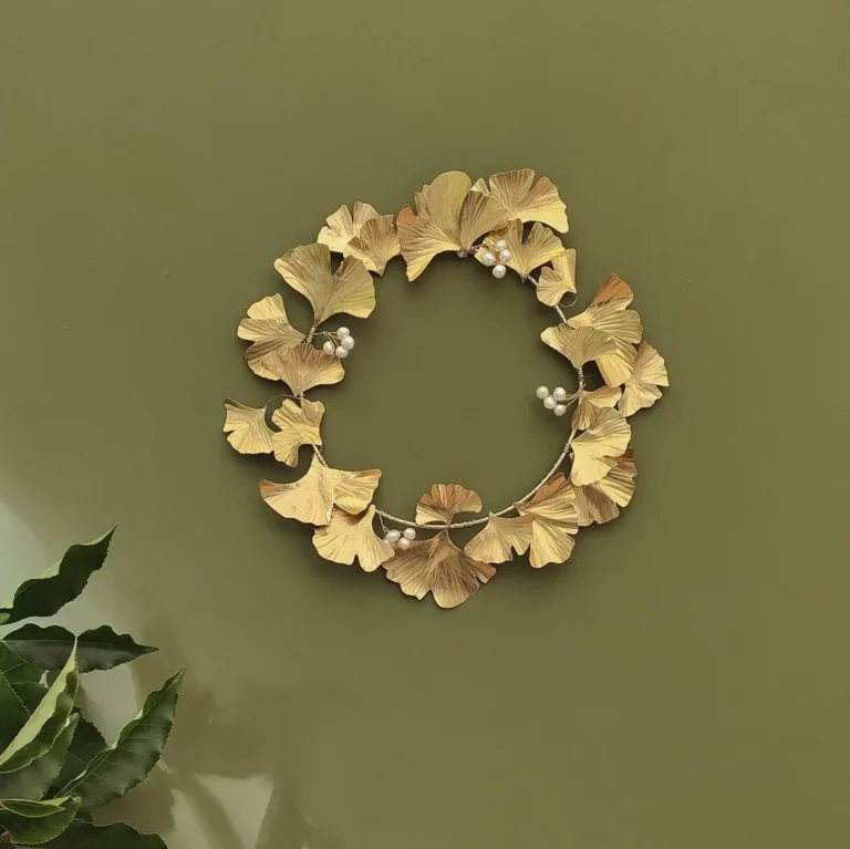 A round gilded leaf wall decoration hangs on an olive green wall.