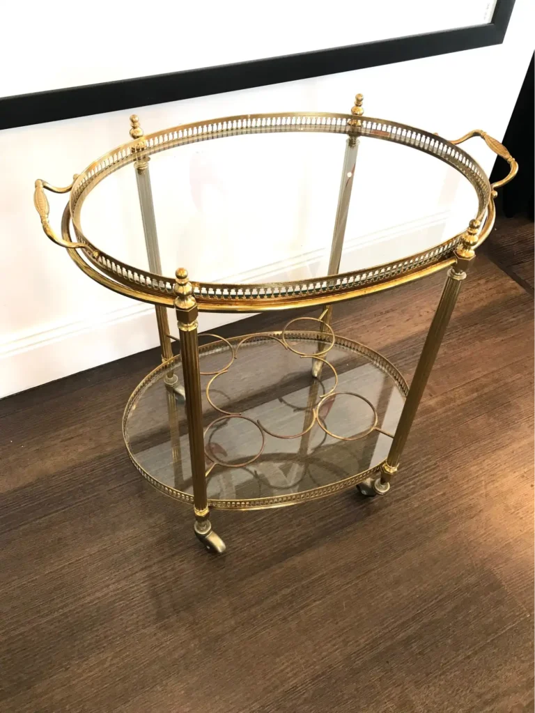 A two-tiered oval-shaped Regency Moderne bar cart with gilded metalwork and opaque surfaces.