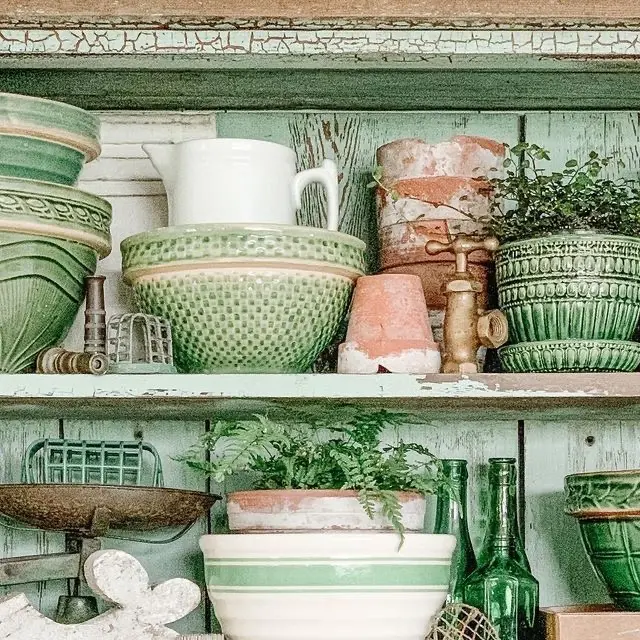 Two shelves with green vintage ceramics, vintage green bottles, an old kitchen scale, and vintage teracotta flower pots.