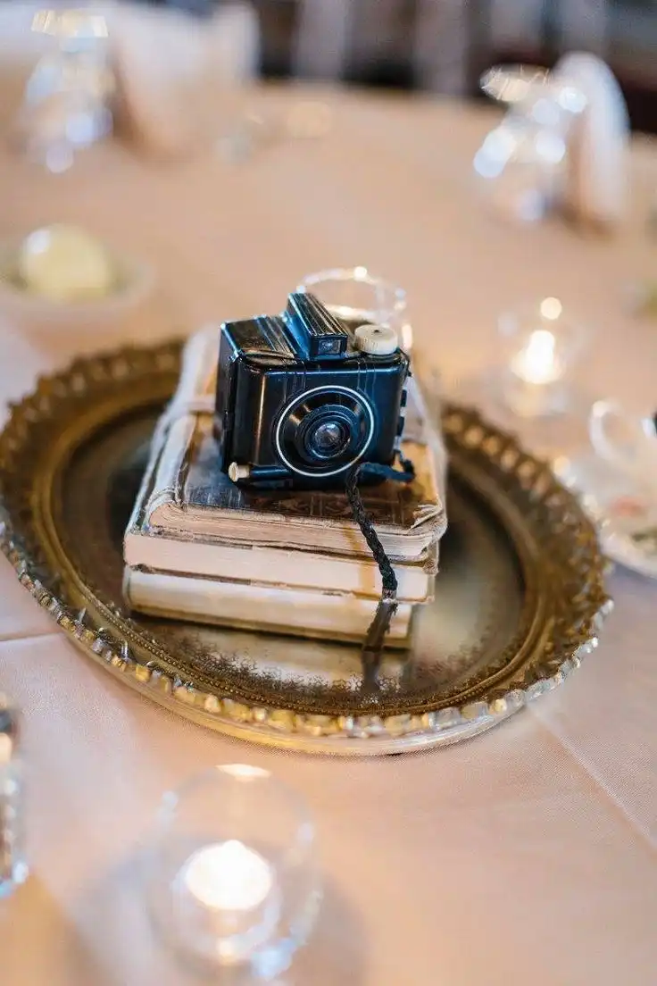 An old Hollywood glam vignette made up of an oval gilded tray with a stack of three books and a vintage camera on top.