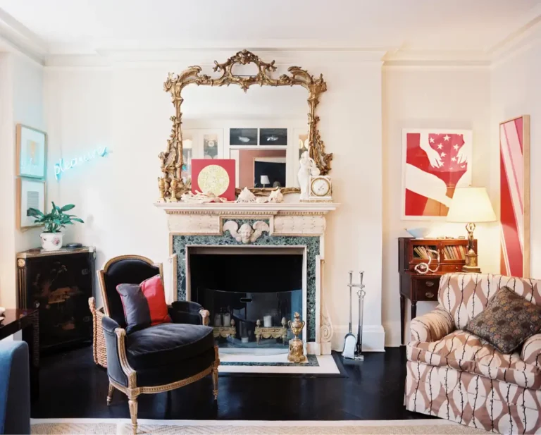 An old Hollywood glamour living room with an ornate Art Deco mantel, black and gold velvet armchair, and a gold ornate mirror.