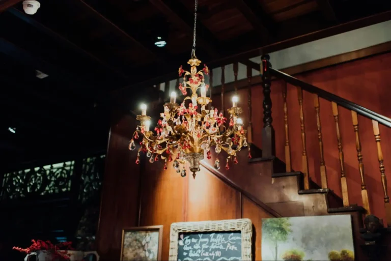 A Murano glass chandelier with clear and pink crystals hangs next to a vintage wooden staircase.