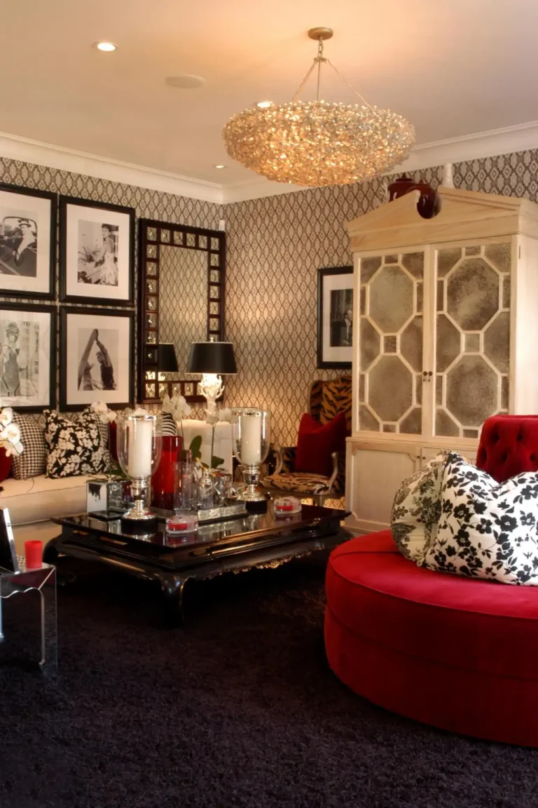 Red tufted velvet furniture, a shaggy black carpet, decorative black coffee table with white candles and other chrome and metallic decorations, an Art Deco style wardrobe, black and white photos of Hollywood stars, a Great Gatsby wallpaper, and a fancy Regency Moderne chandelier.