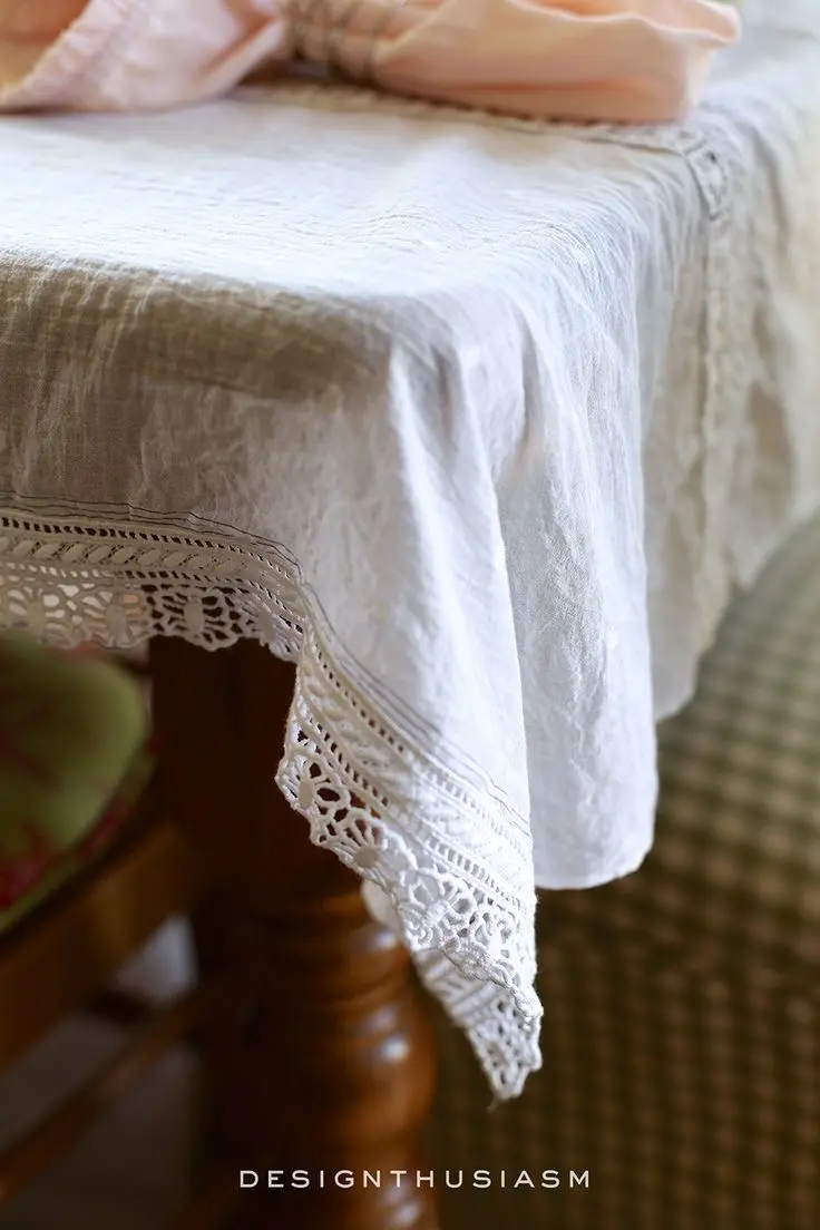 The corner of a dark wooden table covered with a rustic white washed linen tablecloth.