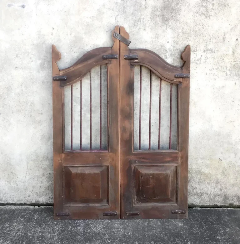 A pair of antique saloon swinging doors stands against a rustic wall outside.