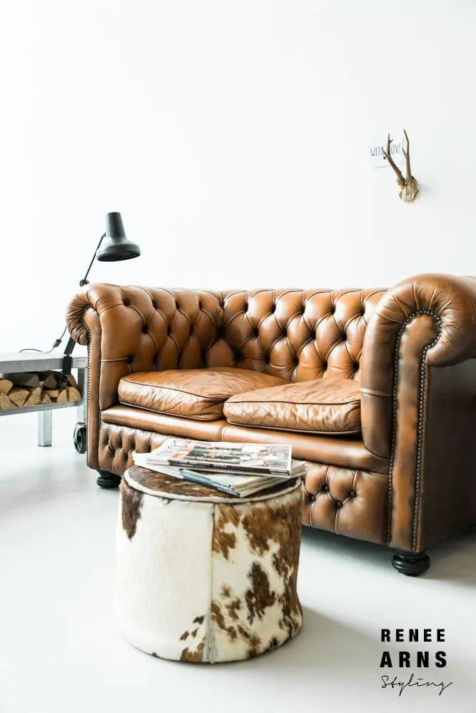 A brown vintage quilted sofa and a cowhide ottoman in an all-white interior.