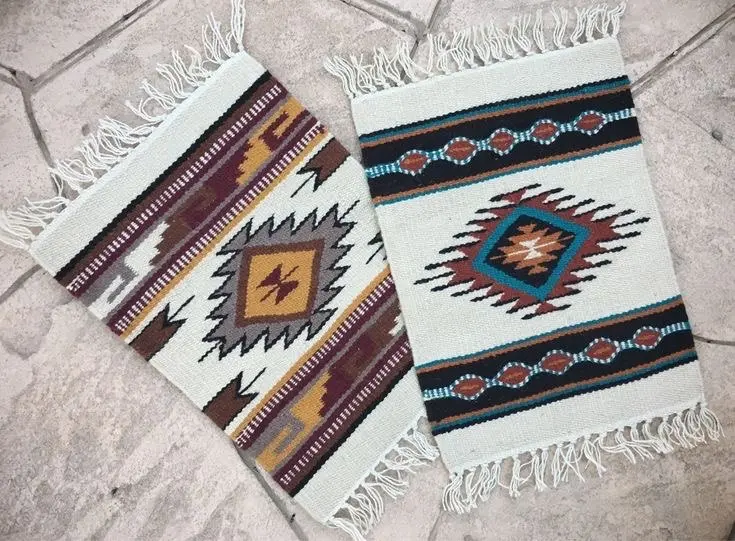 Two woolen placemats with fringes and Native American motifs lie on a light colored tiled floor.