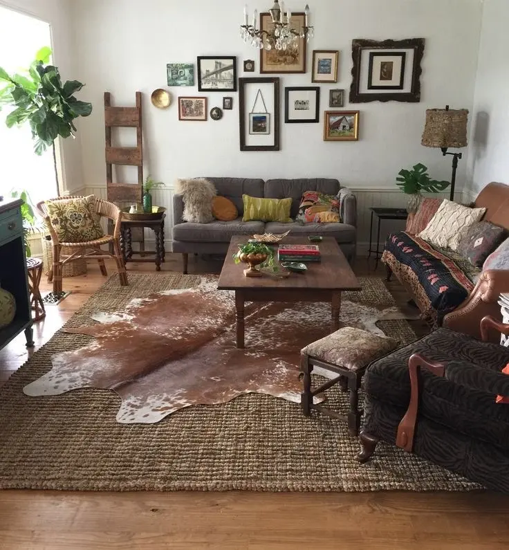 A vintage living room with a cowhide rug, a mid-century table, two couches, a vintage armchair, a rubber plant, a lamp, and a vintage gallery wall.