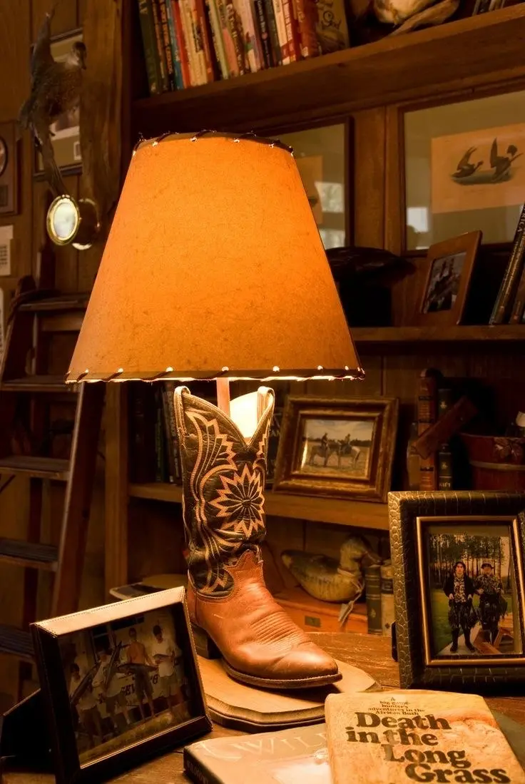 A vintage Old West-style table lamp with a cowboy boot body and a light-colored lamp shade with a leather strap.