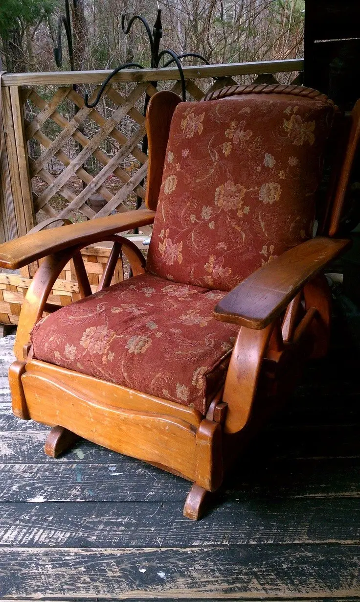 A vintage wagon wheel armchair with floral upholstery stands on a porch with rustic distressed dark wood panels.