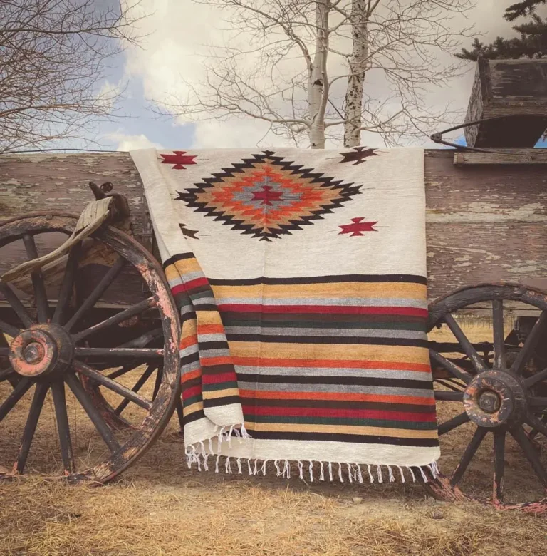 A vintage Wild West decor blanket with fringes and an Aztec motif hangs over a wooden horse carriage.