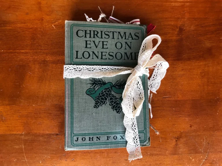 An old book titled Christmas Eve On Lonesome by John Fox Jr. is tied with a white lace cotton ribbon and lies on a worn out wooden surface.