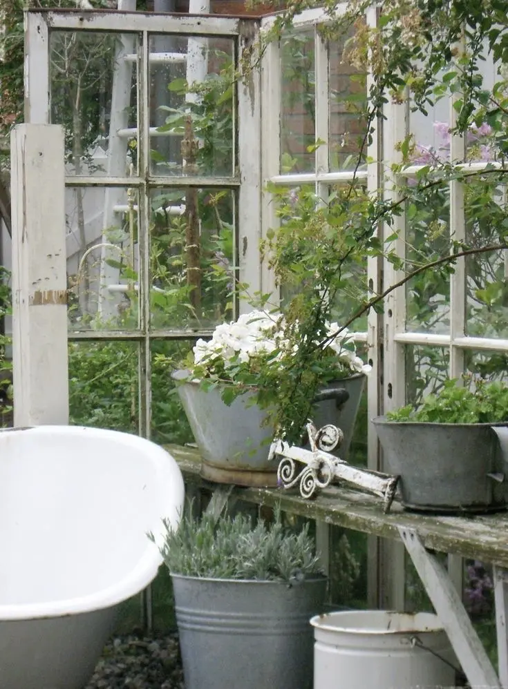 Rustic white French doors in a green garden, enclosing a rustic table with metal pails filled with plants.