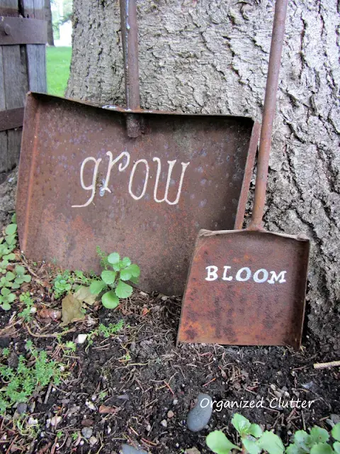 Two distressed and worn out shovels with the words ‘grow’ and ‘bloom’ written in white paint.