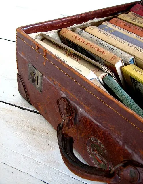 A partial view of a vintage brown leather suitcase on a wooden white surface, filled with old books.