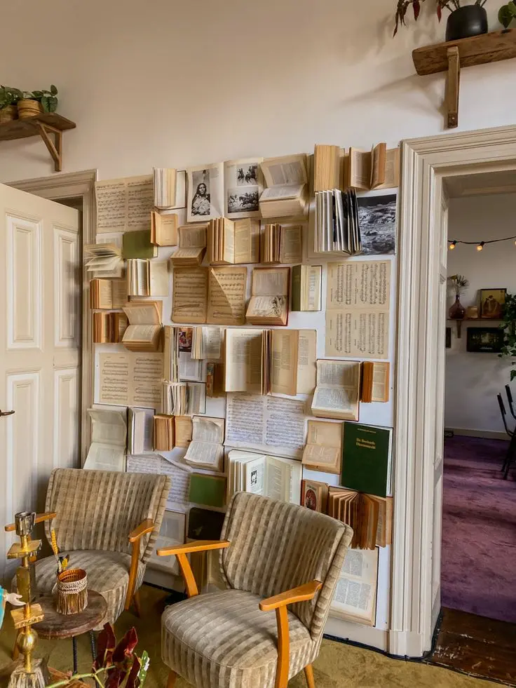 A gallery wall made up of open vintage books hanging on a white wall; two vintage chairs and a small vintage coffee table stand in front of it.