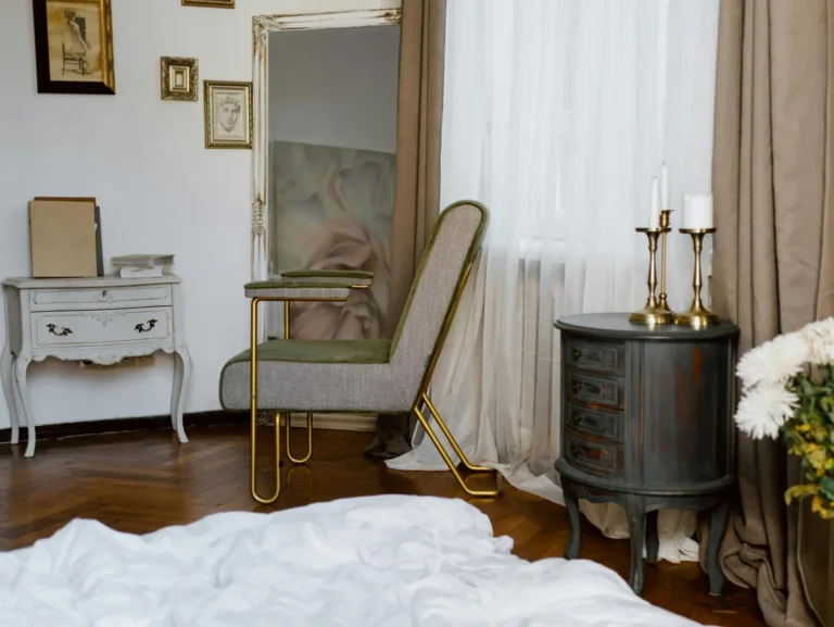 Antique furniture in a vintage Parisian decor interior, featuring two console tables, a vintage armchair, a distressed ornate mirror, classical artwork, and brass candlestick holders.