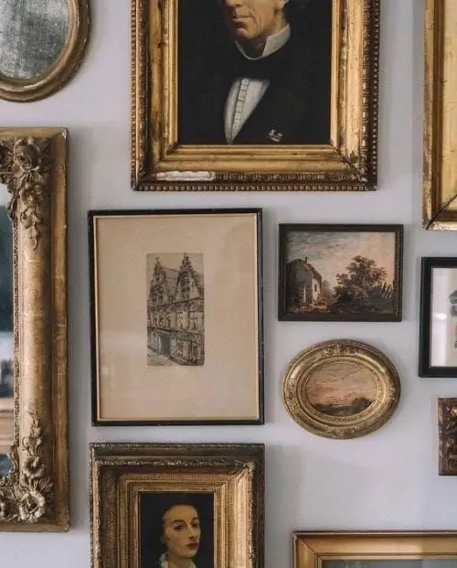 Various classical drawings and oil paintings in ornate rectangular and oval gold frames hang on a wall.